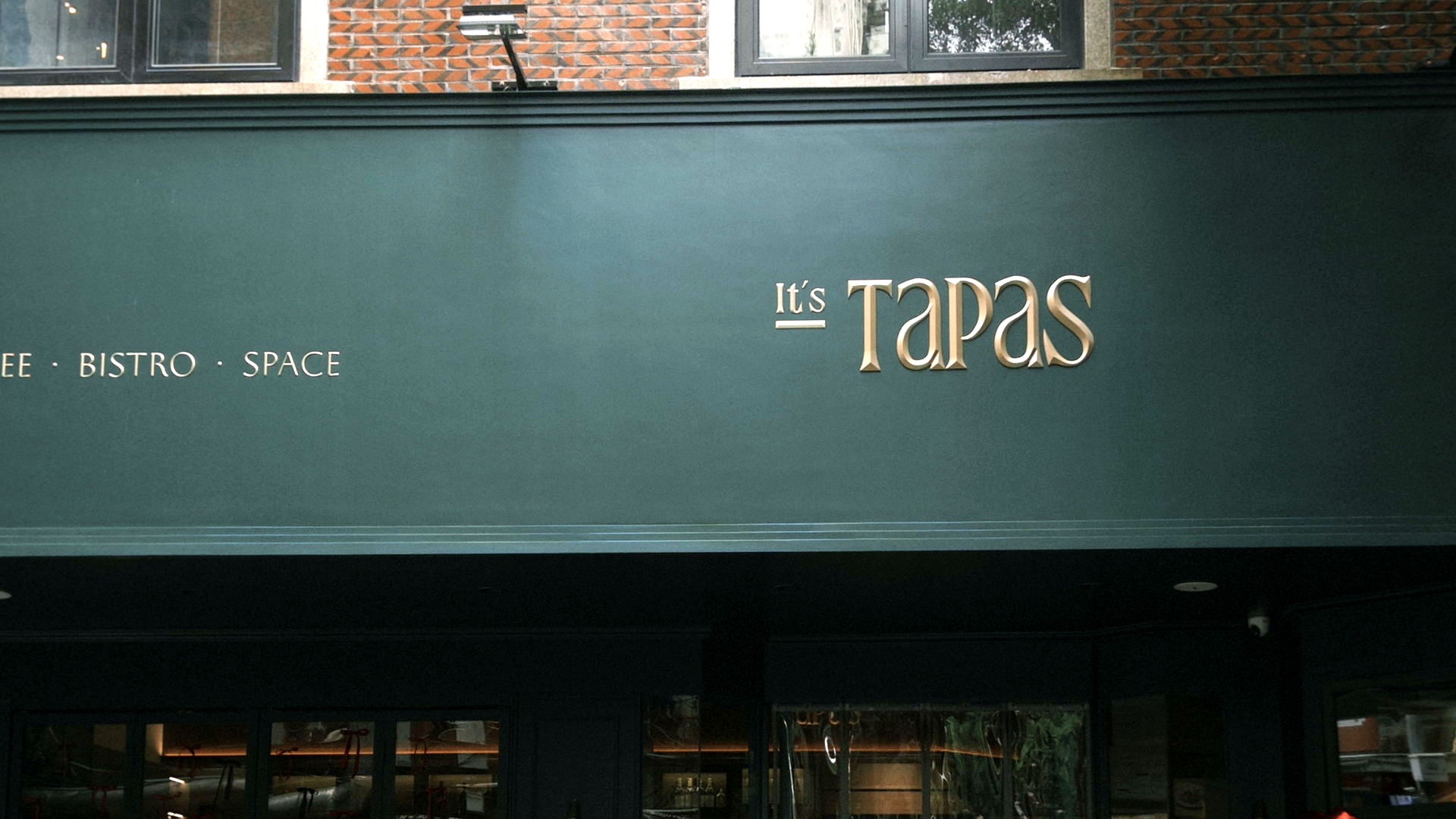It's Tapas storefront: gold lettering on a deep-green wall beneath an old brick facade